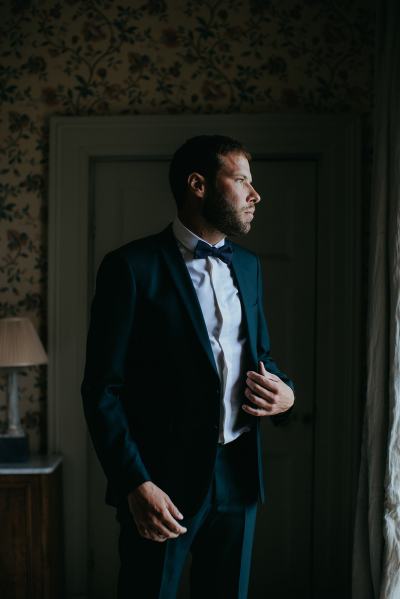 Groom poses and looks out the window he's ready