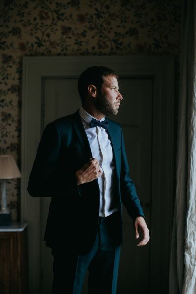 Groom poses and looks out the window he's ready