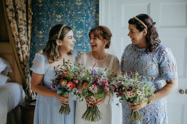 Bride in the middle bridesmaids either side holding bouquet they look at her