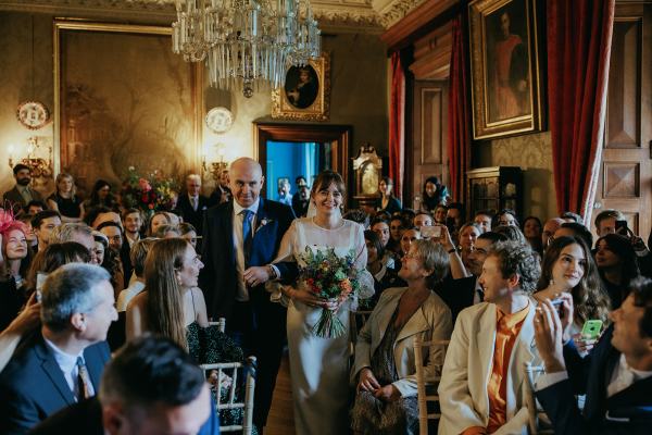 Father of the bride walks daughter down the aisle surrounded by guests