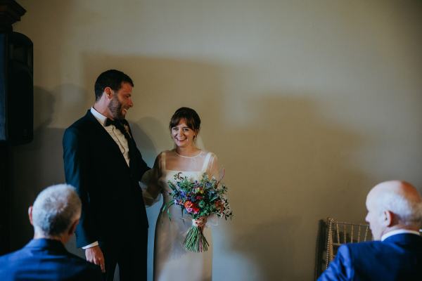 Bride and groom stand at the top of alter in room in front of guests seated