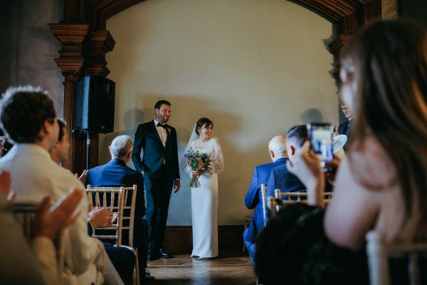 Bride and groom stand at the top of alter in room in front of guests seated