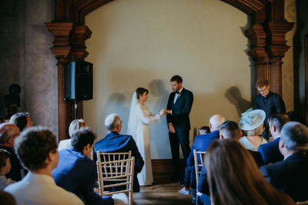 Bride and groom stand at the top of alter in room in front of guests seated