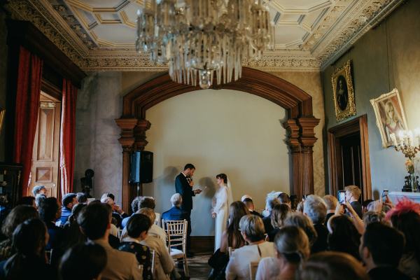 Bride and groom stand at the top of alter in room in front of guests seated