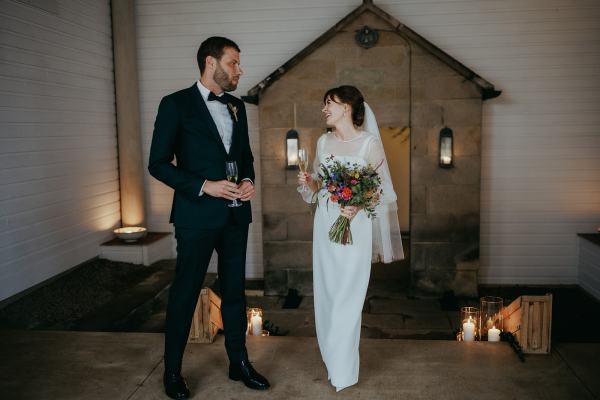 Bride and groom with champagne and glass in hand candles on ground