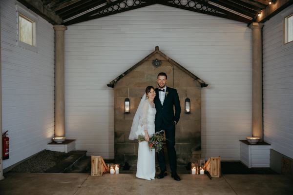 Bride and groom pose candles on ground bouquet in hand