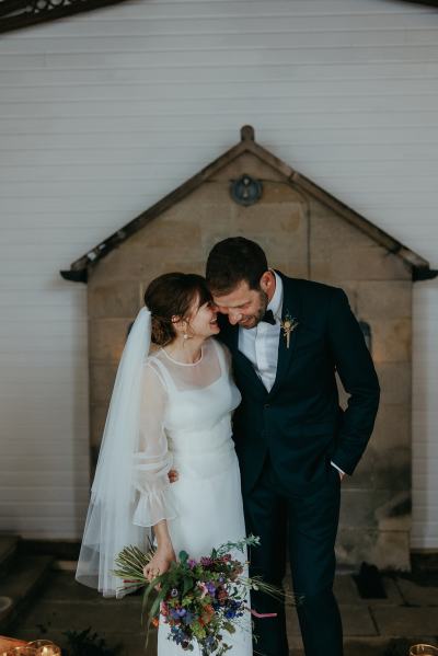 Bride and groom pose candles on ground bouquet in hand bride smiles laughs