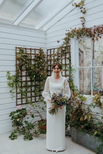 Bride poses in greenhouse on her own holding bouquet flowers