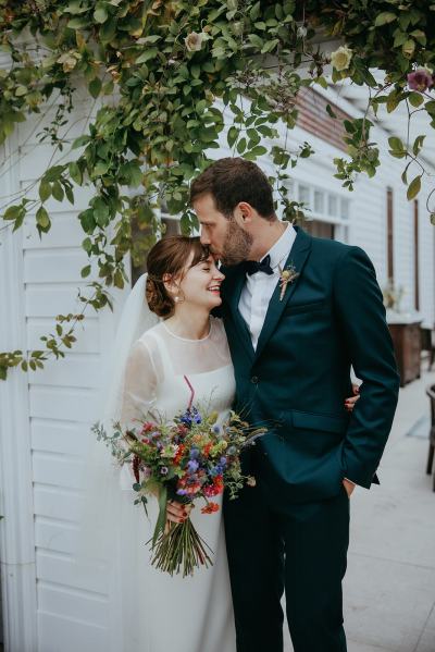 Groom kisses bride on forehead ivy in background