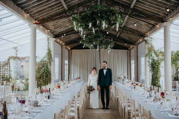 Bride and groom standing in dining room together flower chandelier ahead