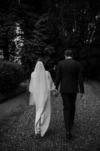 Bride and groom from behind walking hand in hand holding hands black and white shot