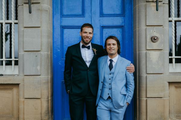 Groom and groomsman in blue suit pose in front of blue door entrance