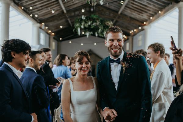 Bride and groom enter ballroom with guests clapping they throw confetti on couple