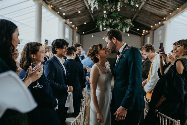 Bride and groom enter ballroom with guests clapping they throw confetti on couple as they kiss