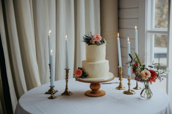 White wedding cake with flowers candles lit on table and stand