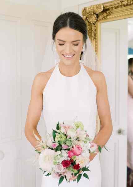 Bride shows off her hair and makeup as she's getting ready by looking down towards her flowers/bouquet