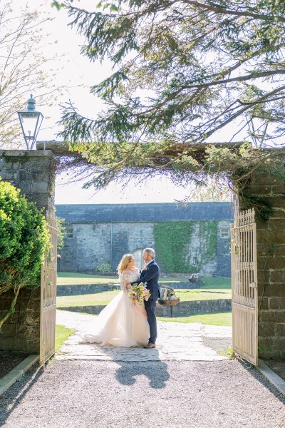 Bride and groom stand holding each other under archway