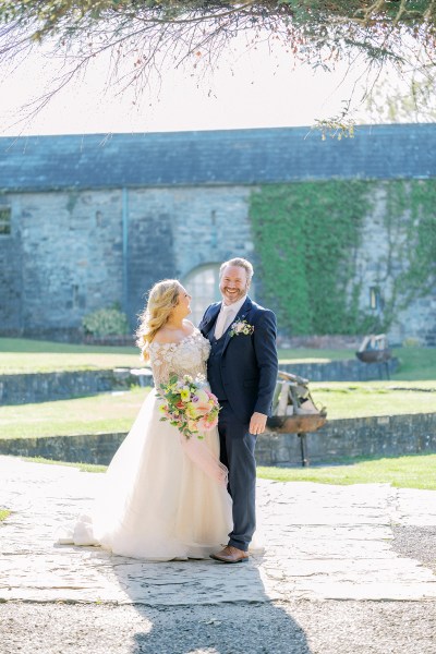 Bride looks at her groom as they stand in garden