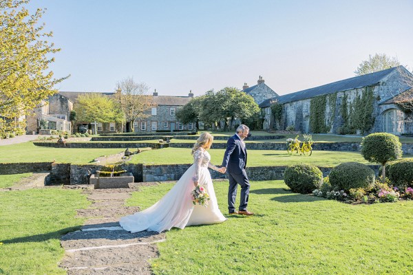 Bride and groom holding hands on the grass sunshine