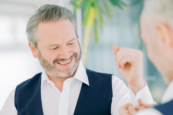 Groom gets help from groomsman with shirt