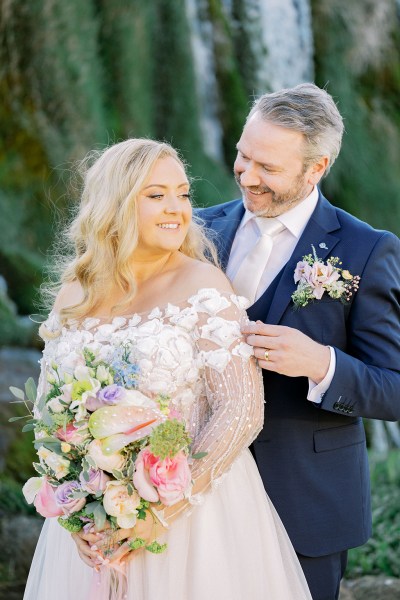 Groom stands behind bride and smiles at her