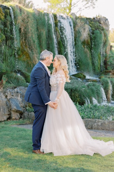 Bride and groom face each other in front of waterfall