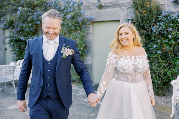 Bride and groom walking hand in hand in courtyard smiling