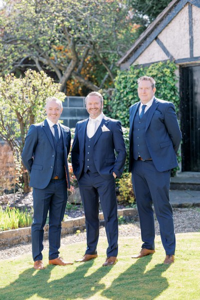 Groom and groomsmen pose outside on the grass in garden sunshine