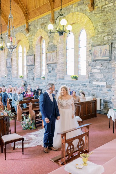 Bride and groom smile holding hands at alter smiling