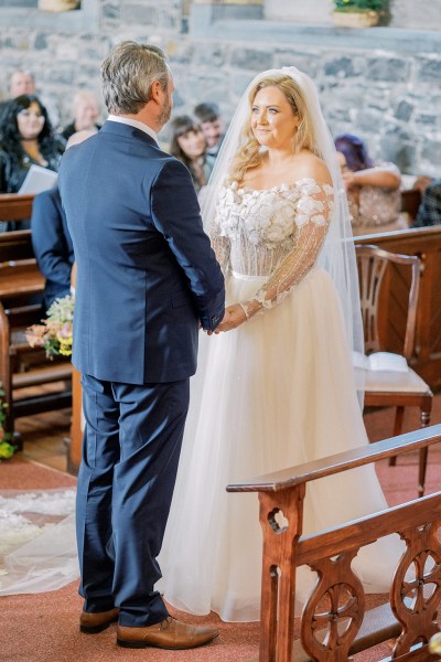 Bride and groom smile holding hands at alter smiling