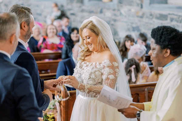 Bride smiles as she puts ring on grooms finger