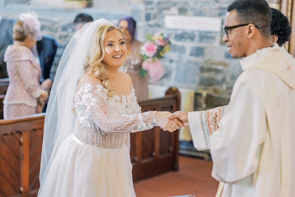 Bride holds hands with priest in church