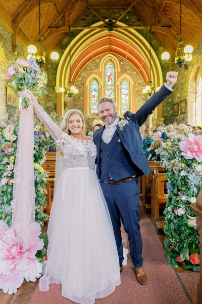 Bride and groom celebrate wedding hands in the air bouquet church setting