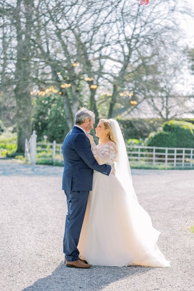 Bride and groom face each other smiling happy in forest fence in background