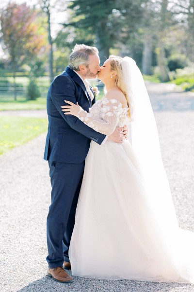 Bride and groom kiss in the sunshine on pathway