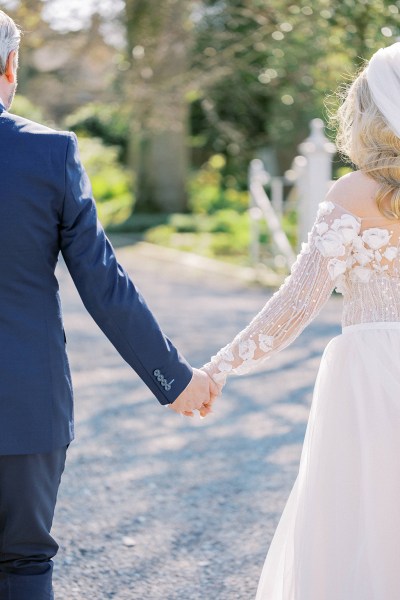 Bride and groom walk hand in hand from behind walking on pathway