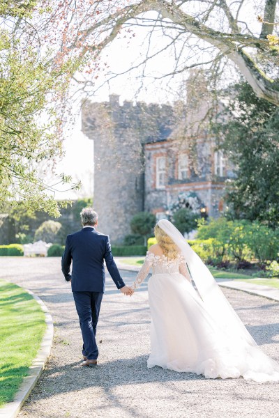 Bride and groom walk hand in hand from behind