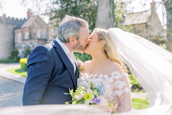 Groom kisses bride as veil blows in the wind