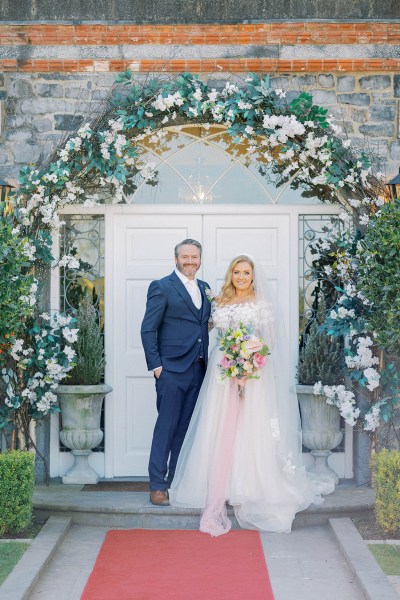 Bride and groom smile at entrance to wedding venue