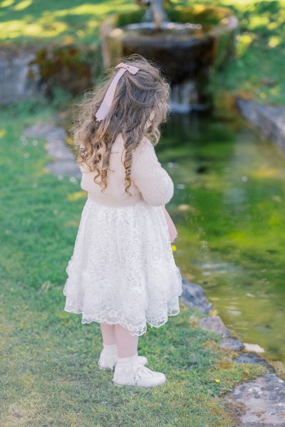 Little girl looking down at the pond wearing white dress