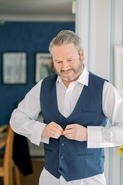 Groom puts on his waistcoat over white shirt