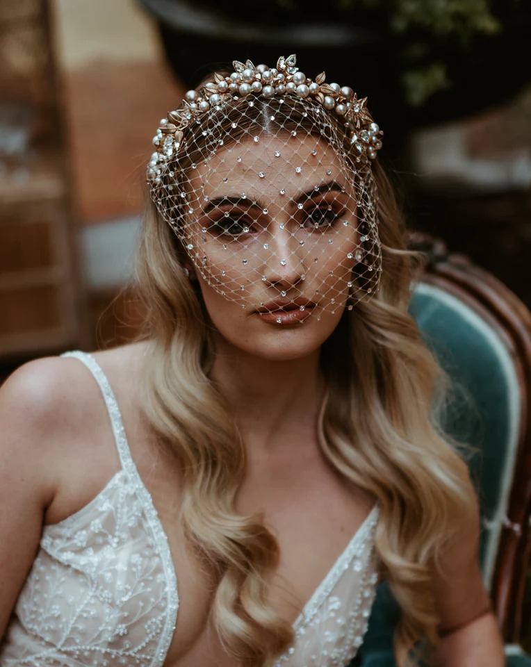 A bride sits on a blue leather chair wearing a lace wedding dress and veil