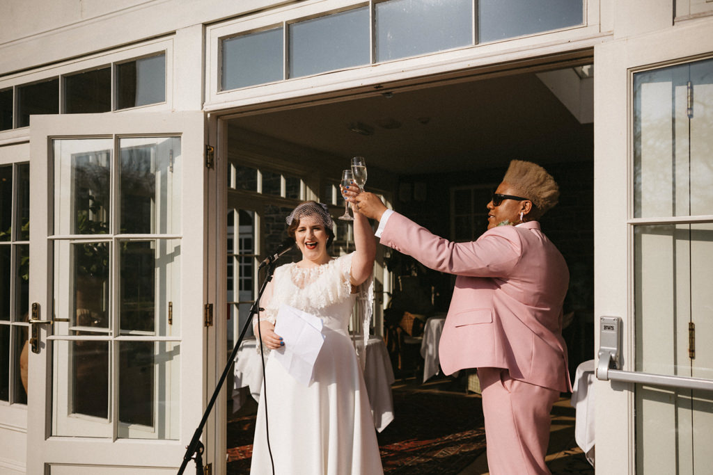 Two brides hold hands up in the air