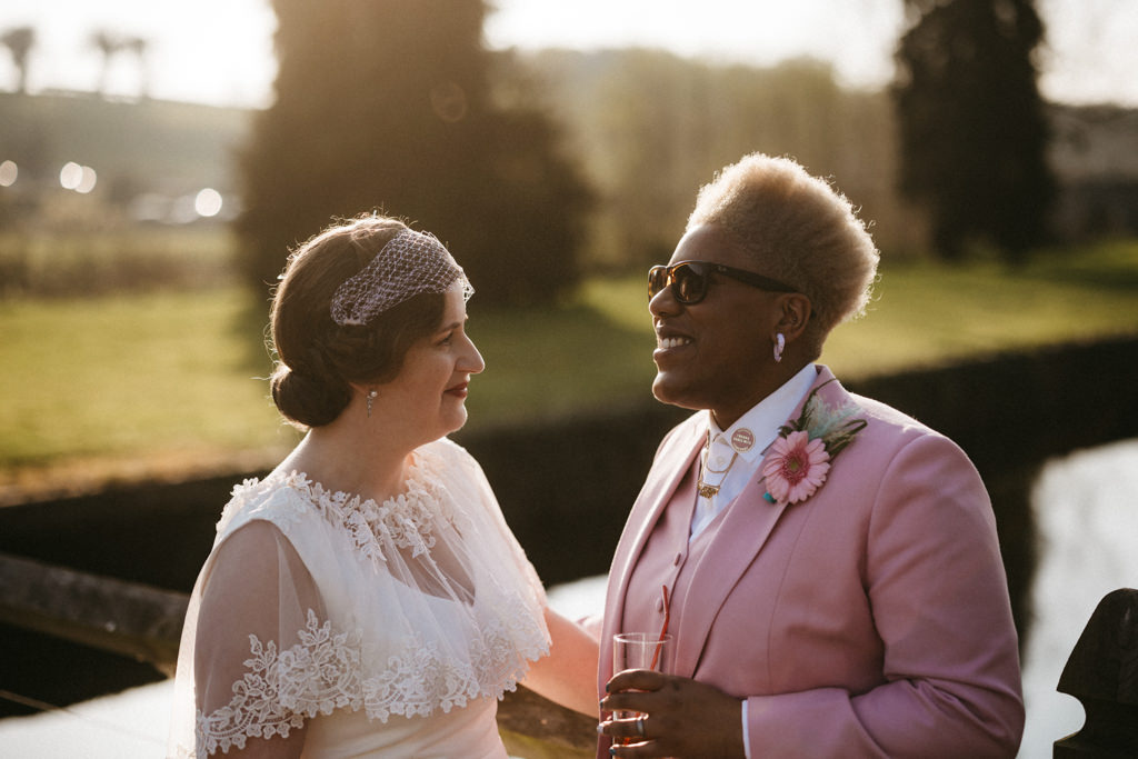 Two brides smile greenery in backgrounds trees on bridge