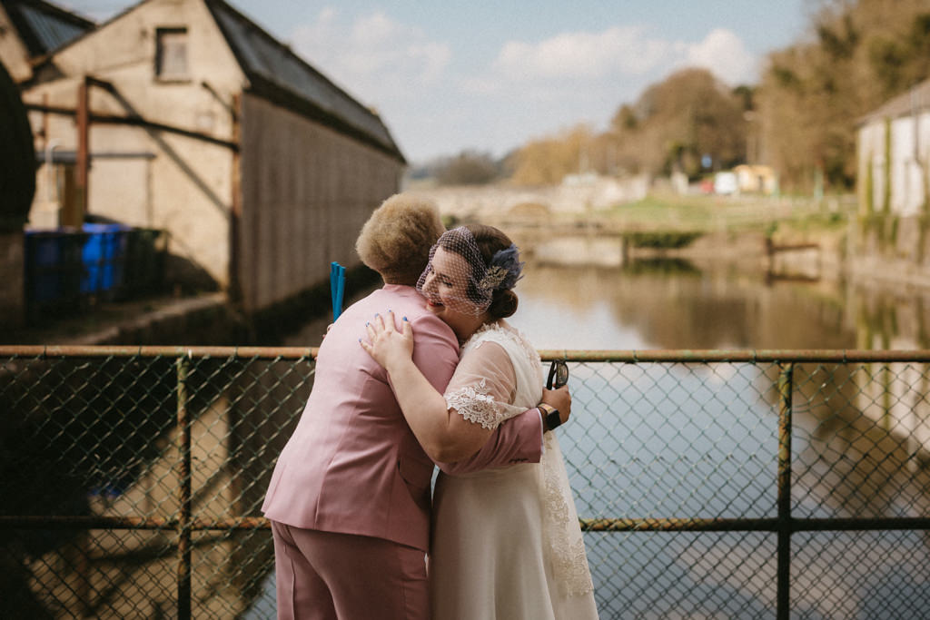 Brides hug on bridge overlooking lake in background