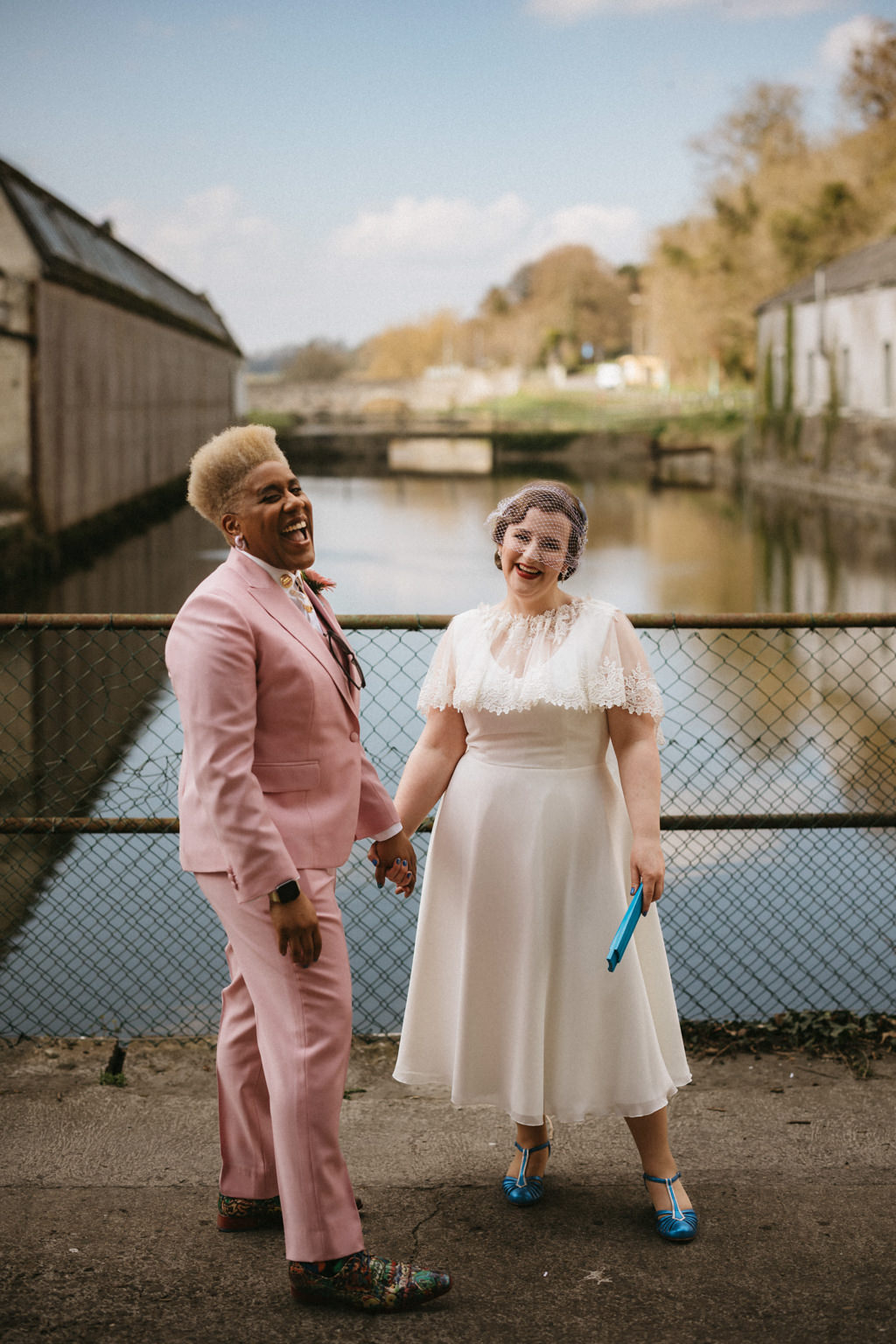 Brides hold hands on bridge lake in background