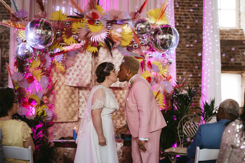 Two brides clap kiss at alter disco ball colourful setting