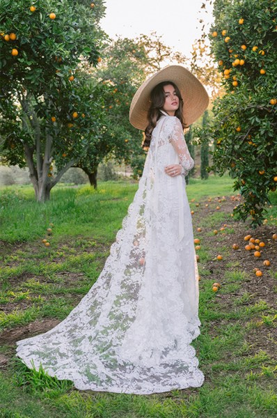 Monique Lhuillier Spring 2024 Collection bride stands in garden long lace dress straw hat