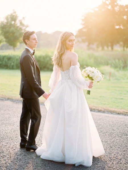 Bride and groom walk along the pathway to wedding venue bride looks over her shoulder