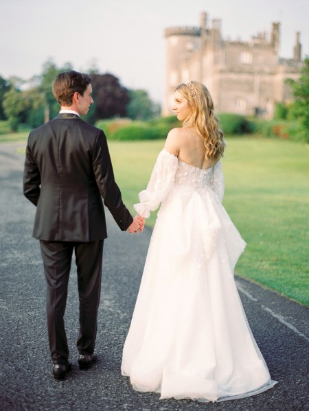 Bride and groom walk along the pathway to wedding venue bride looks over her shoulder